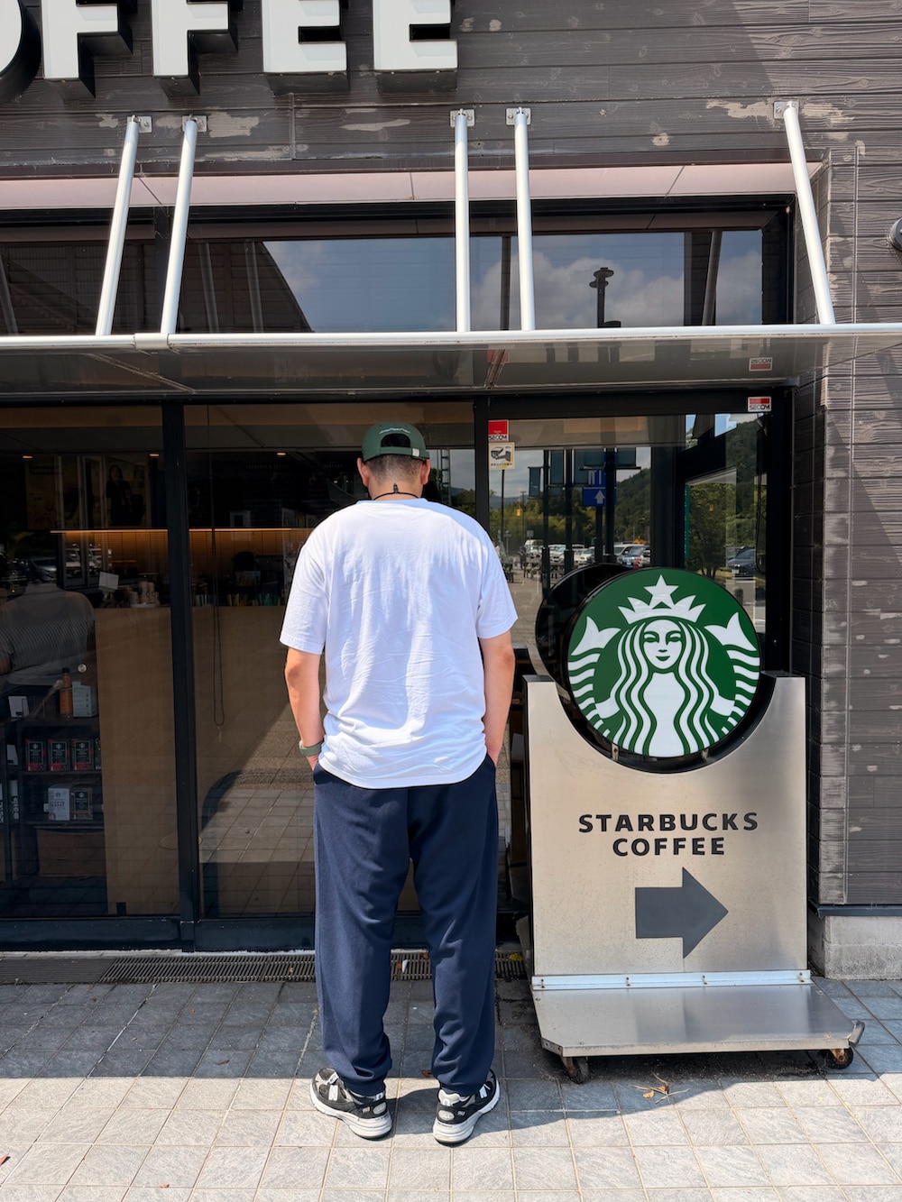 ホワイト系のTシャツ/カットソー、ブルー系のスラックス、ブラック系のスニーカーを着用したメンズの夏コーディネートの2枚目の写真