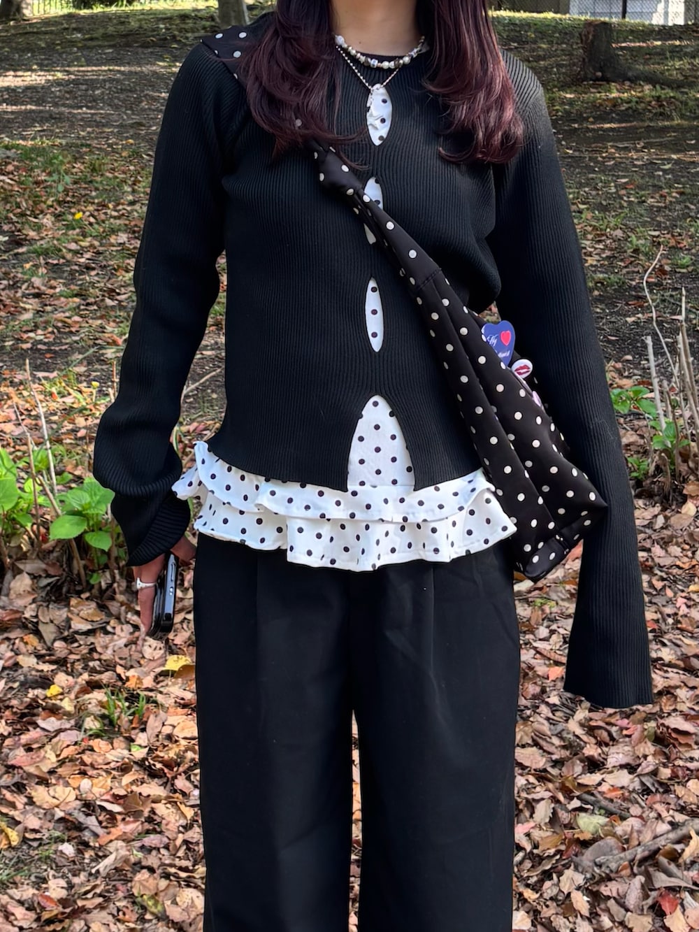 ホワイト系のトップス、ブラック系のニット/セーター、ブラック系のショルダーバッグを着用したレディースの春コーディネートの2枚目の写真