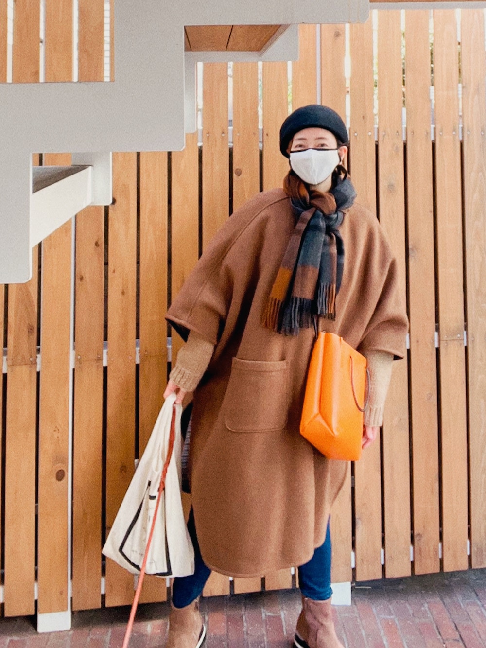 ブラウン系のポンチョ、オレンジ系のショルダーバッグ、ホワイト系のエコバッグ/サブバッグを着用したレディースの冬コーディネートの4枚目の写真