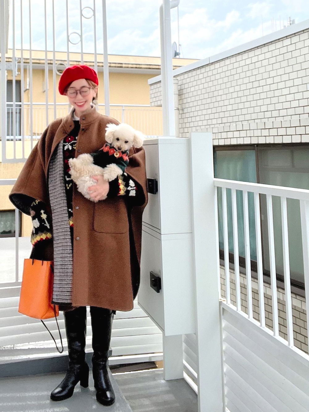 ブラウン系のポンチョ、ブラック系のニット/セーター、オレンジ系のショルダーバッグを着用したレディースの冬コーディネートの2枚目の写真