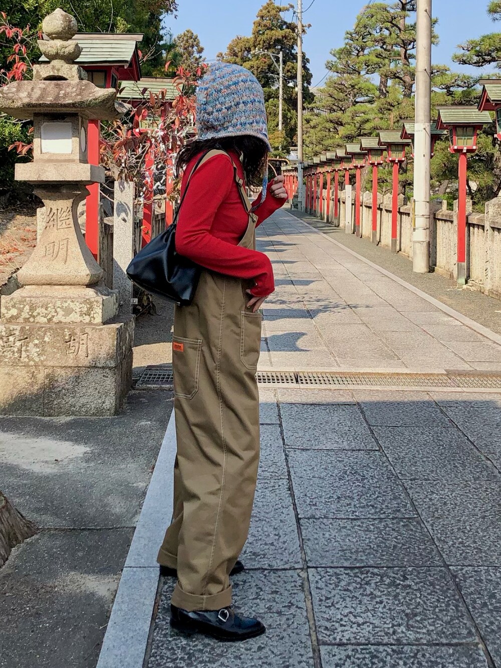 レッド系のニット/セーター、ベージュ系のサロペット/オーバーオール、ブラック系のショルダーバッグを着用したレディースの秋コーディネートの2枚目の写真