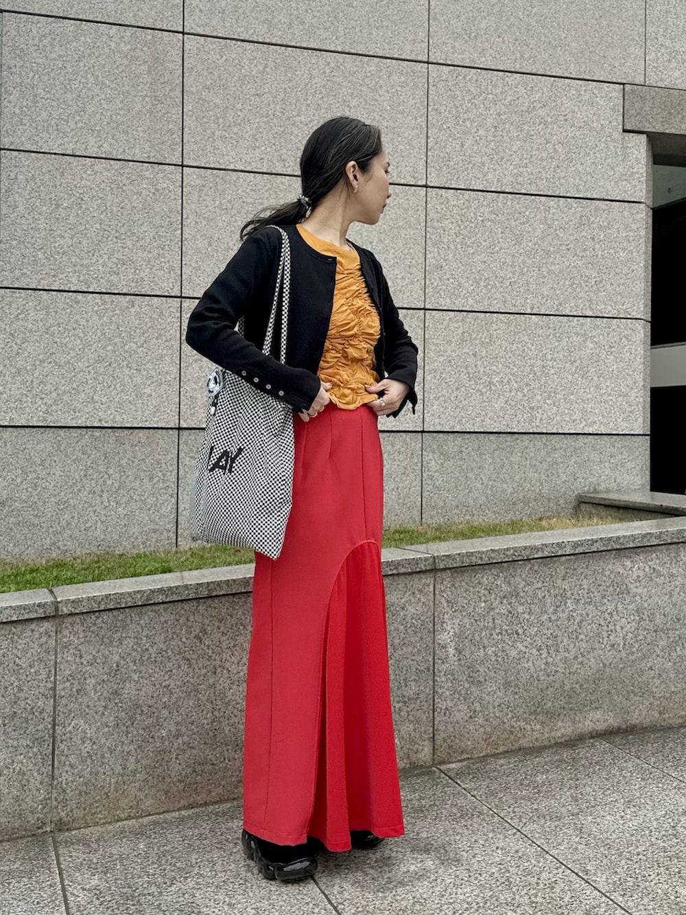 ブラック系のカーディガン/ボレロ、オレンジ系のTシャツ/カットソー、レッド系のスカートを着用したレディースの春コーディネートの2枚目の写真