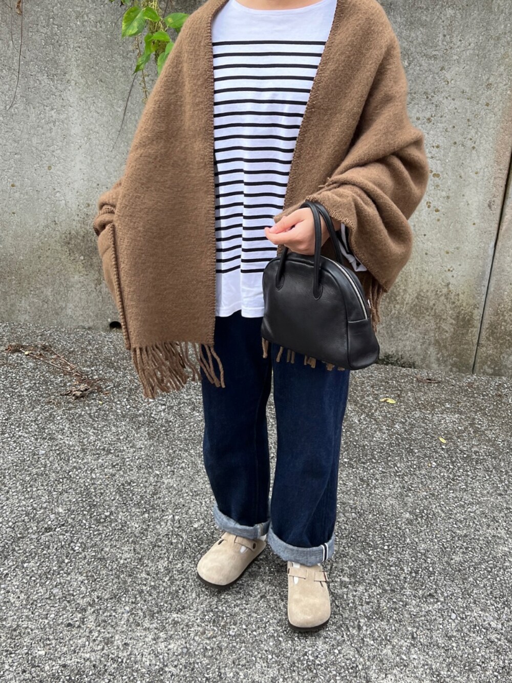 ブラック系のバッグ、ブルー系のデニムパンツ、ベージュ系のサンダルを着用したレディースの秋コーディネートの3枚目の写真