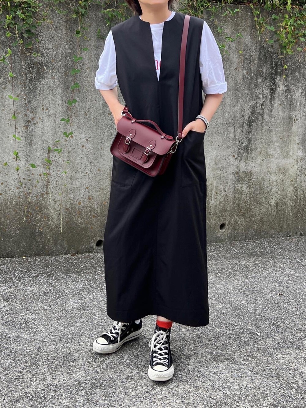 ブラウン系のショルダーバッグ、ブラック系のジャンパースカート、ブラック系のスニーカーを着用したレディースの秋コーディネートの3枚目の写真