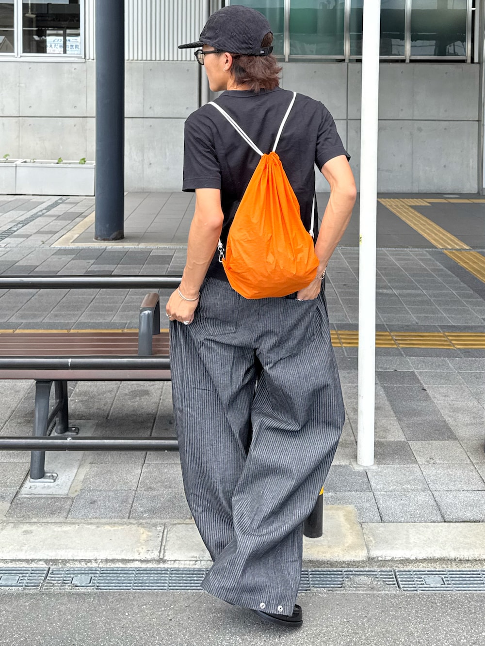 ブラック系のローファー、オレンジ系のバックパック/リュック、ブラック系のキャップを着用したメンズの夏コーディネートの2枚目の写真