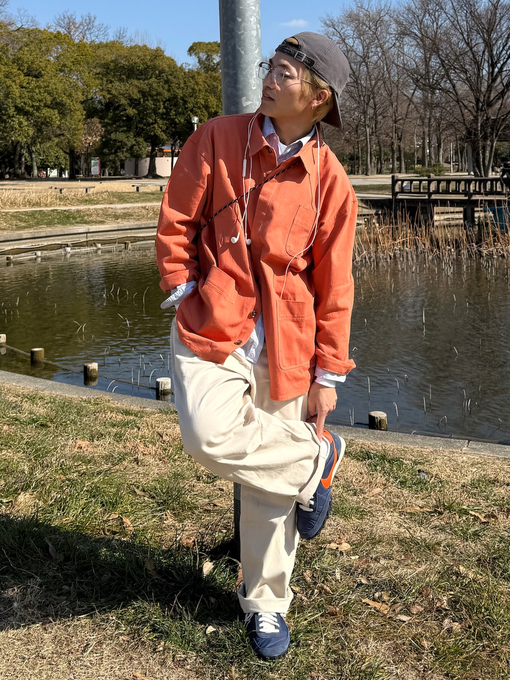 オレンジ系のトップス、ベージュ系のチノパンツ、ブルー系のスニーカーを着用したメンズの冬コーディネートの2枚目の写真