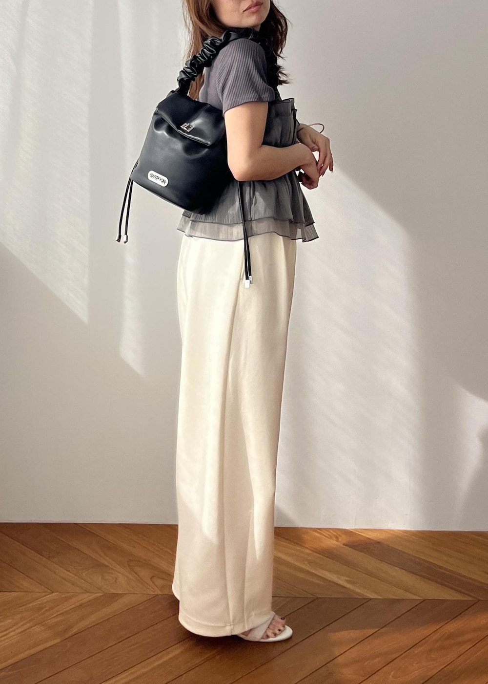 ホワイト系のスラックス、ブラック系のショルダーバッグ、ホワイト系のサンダルを着用したレディースの春コーディネートの3枚目の写真