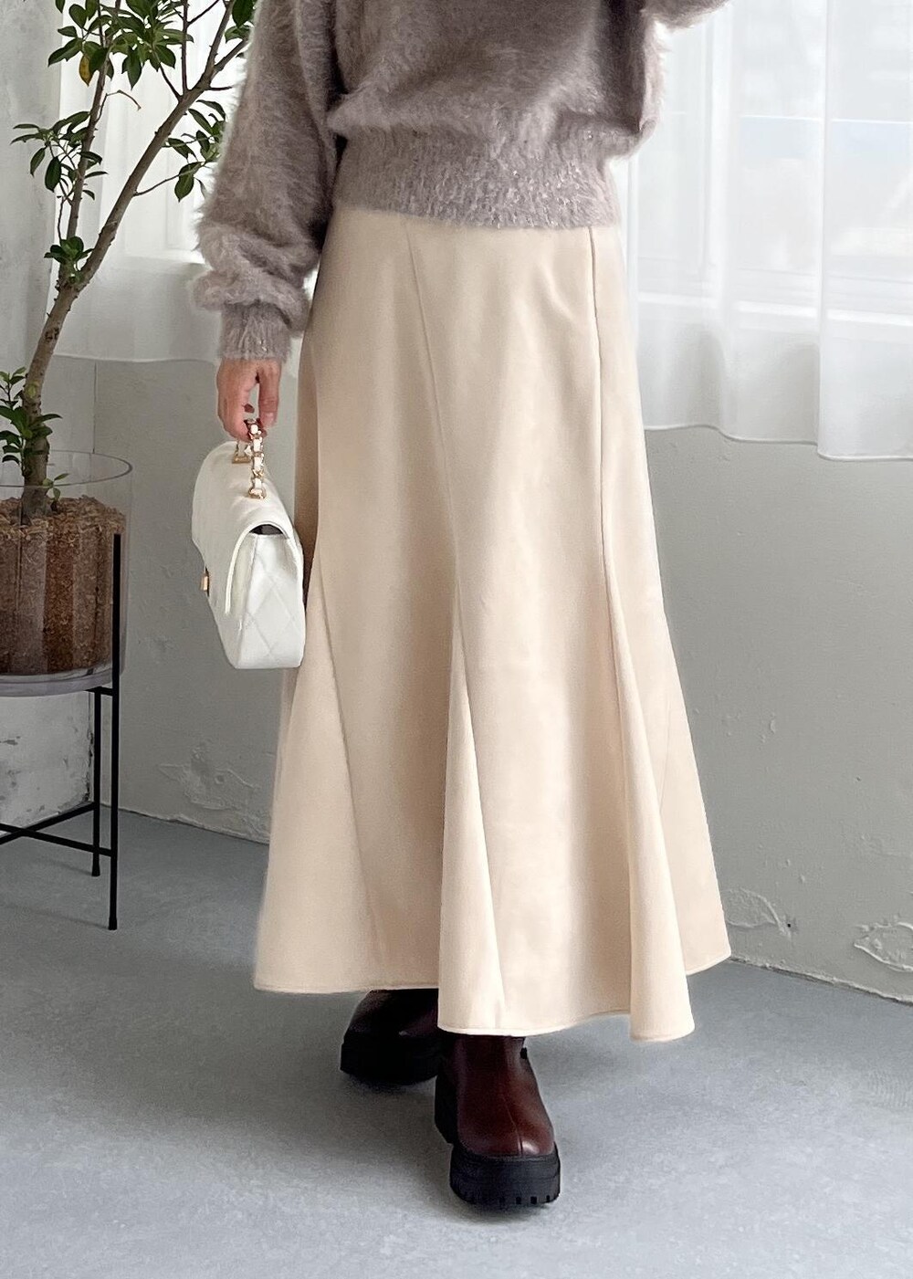 ブラウン系のブーツ、ホワイト系のスカート、ベージュ系のニット/セーターを着用したレディースの秋コーディネートの2枚目の写真