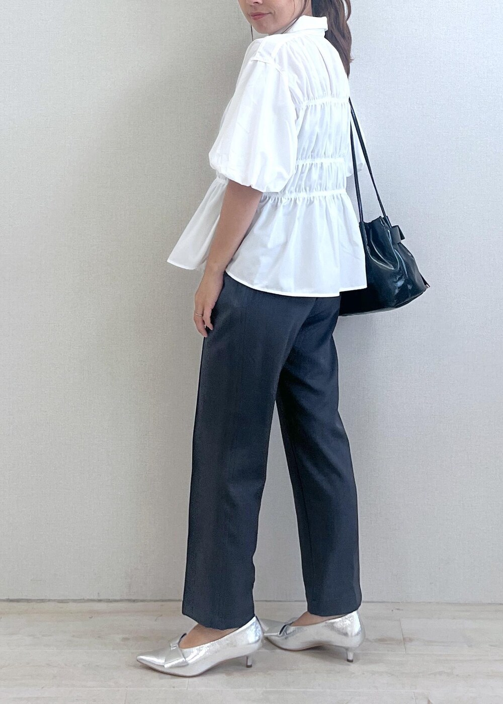 シルバー系のパンプス、ブラック系のショルダーバッグ、グレー系のスラックスを着用したレディースの秋コーディネートの2枚目の写真