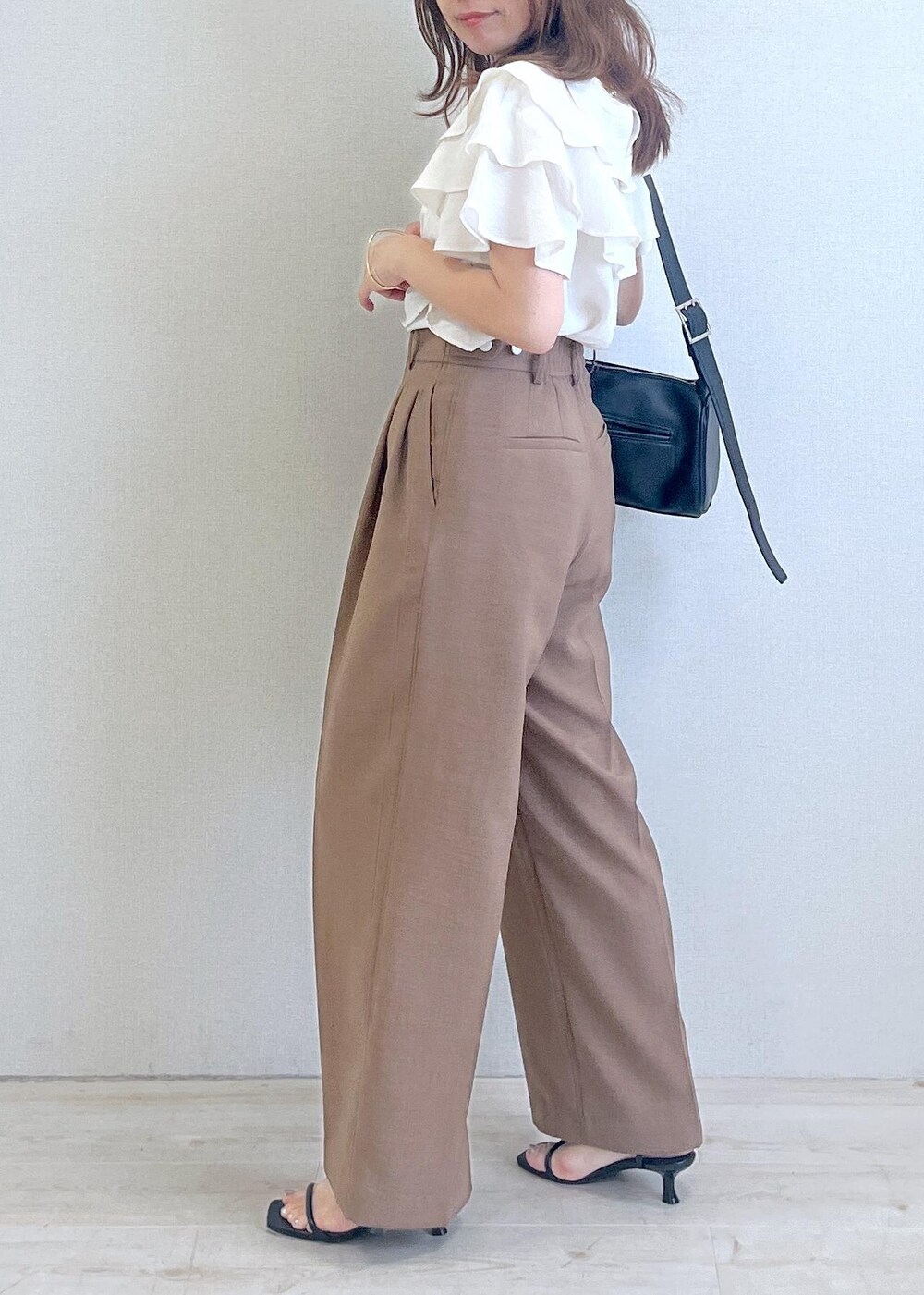 ブラック系のショルダーバッグ、ブラック系のサンダル、ブラウン系のスラックスを着用したレディースの夏コーディネートの2枚目の写真