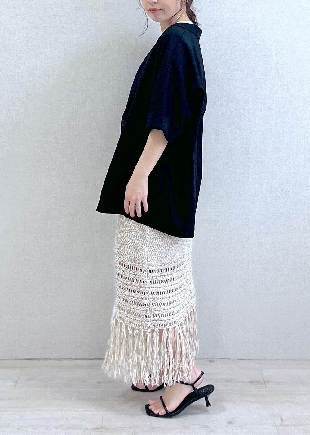 シルバー系のハンドバッグ、ベージュ系のスカート、ブラック系のサンダルを着用したレディースの春コーディネートの2枚目の写真