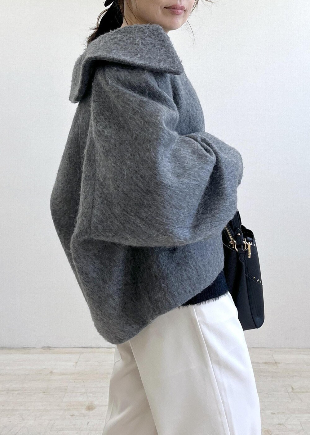 グレー系のブルゾン、ホワイト系のスラックス、ブラック系のニット/セーターを着用したレディースの冬コーディネートの6枚目の写真