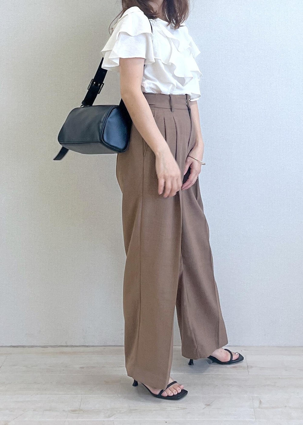 ブラック系のショルダーバッグ、ブラック系のサンダル、ブラウン系のスラックスを着用したレディースの夏コーディネートの3枚目の写真