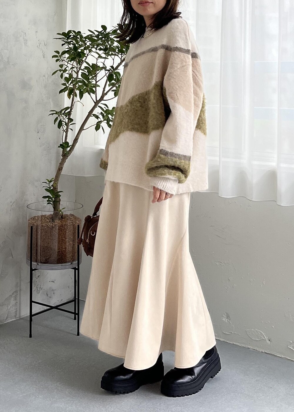 ブラウン系のボストンバッグ、ブラック系のブーツ、ホワイト系のスカートを着用したレディースの秋コーディネートの3枚目の写真