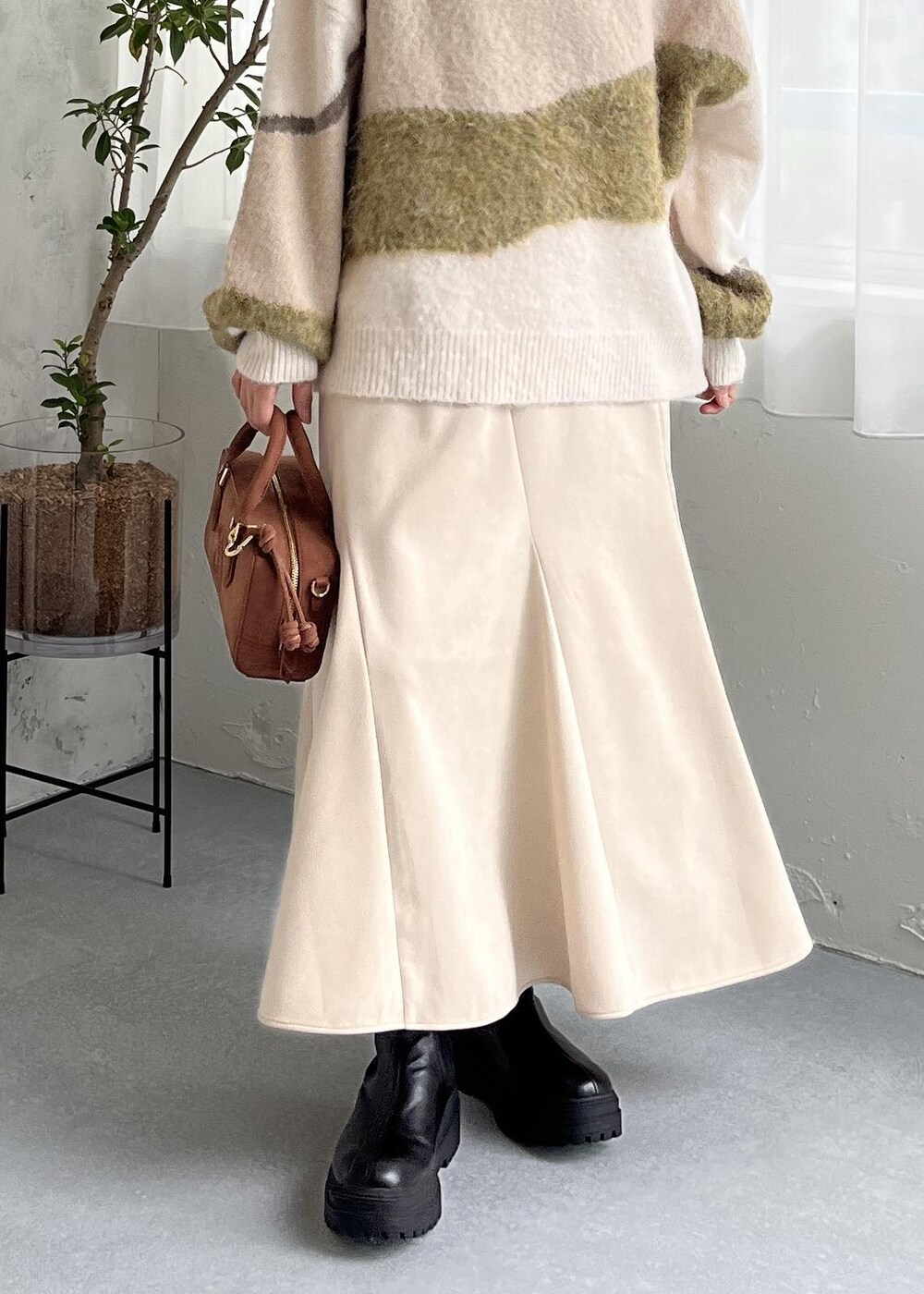 ブラウン系のボストンバッグ、ブラック系のブーツ、ホワイト系のスカートを着用したレディースの秋コーディネートの9枚目の写真