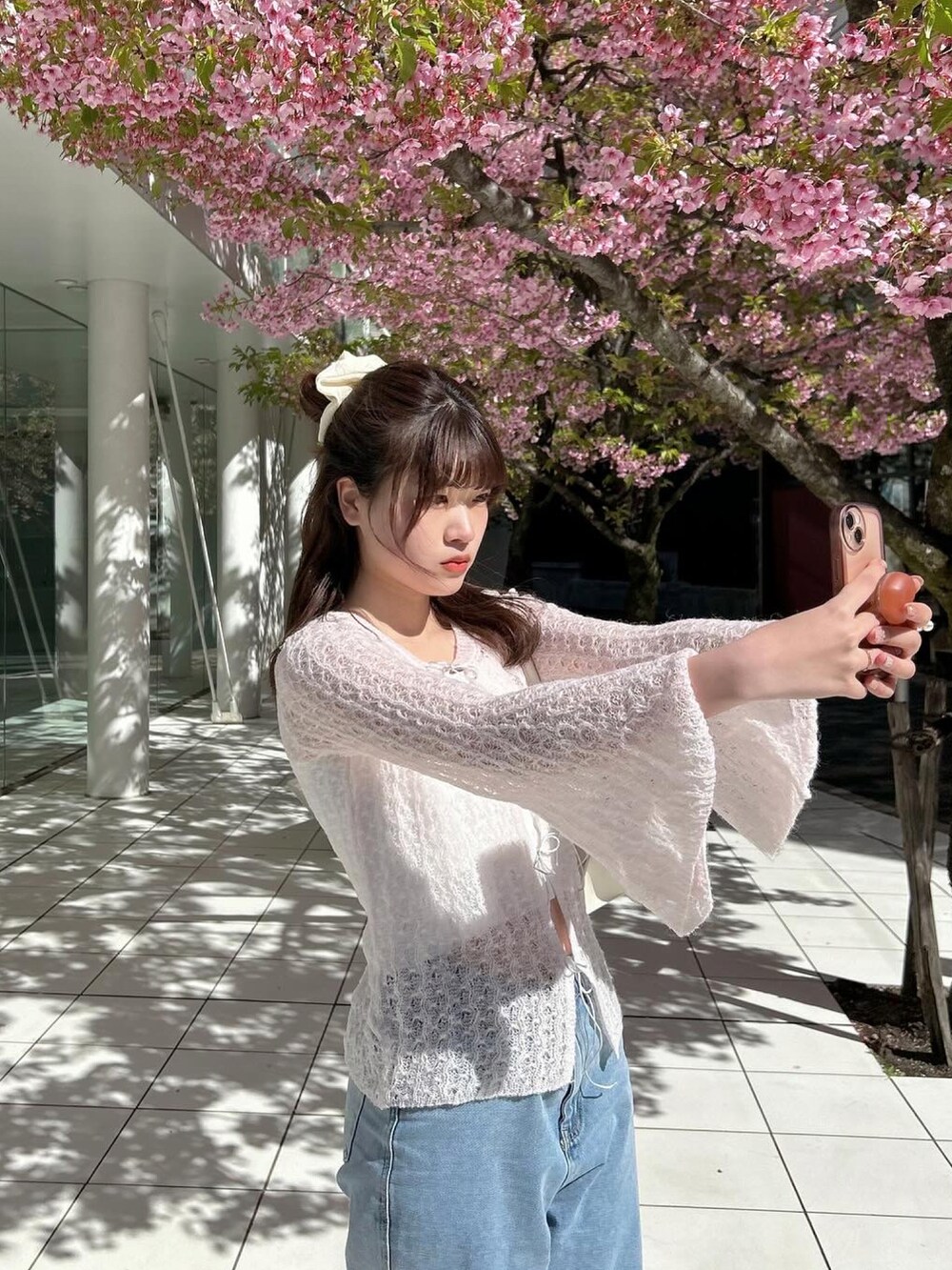 ブルー系のデニムパンツ、ピンク系のニット/セーター、ホワイト系のスニーカーを着用したレディースの春コーディネートの3枚目の写真