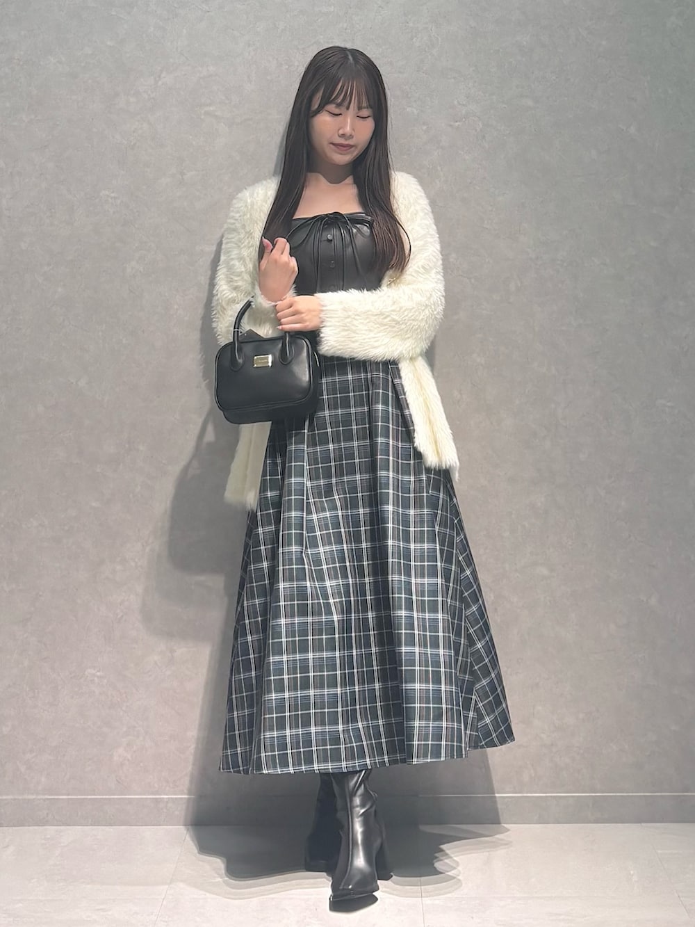 グリーン系のワンピース、ブラック系のハンドバッグ、ブラック系のブーツを着用したレディースの秋コーディネートの2枚目の写真