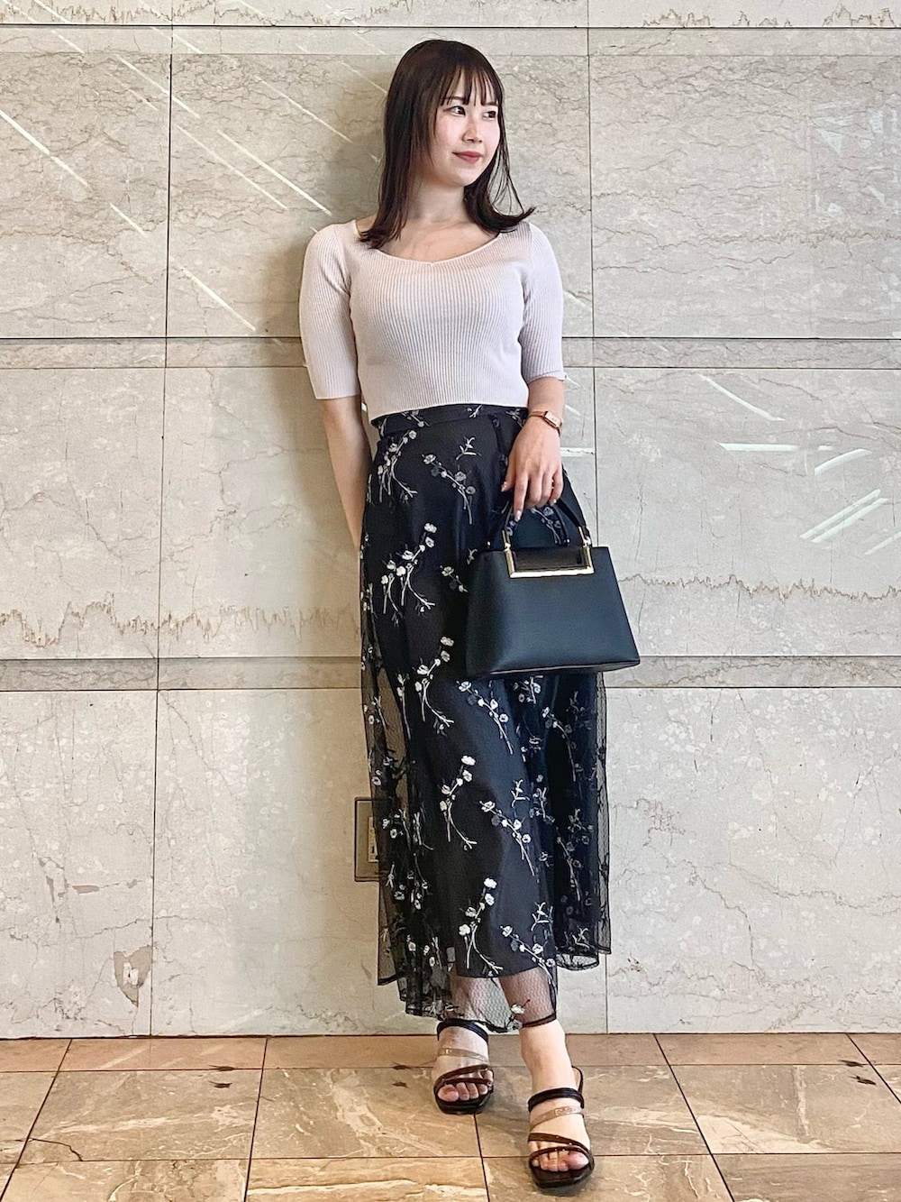ブラック系のハンドバッグ、グレー系のスカート、ブラック系のサンダルを着用したレディースの春コーディネートの2枚目の写真