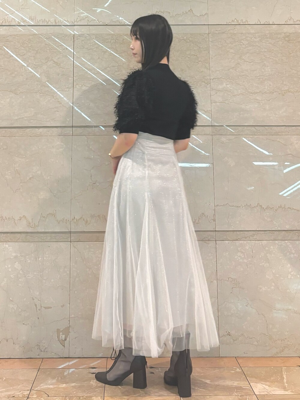 ホワイト系のスカート、ブラウン系のブーツ、ブラック系のニット/セーターを着用したレディースの秋コーディネートの2枚目の写真