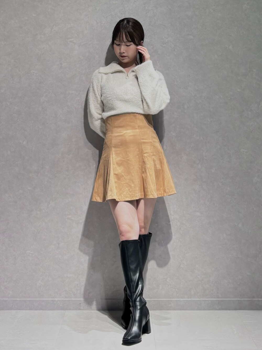 イエロー系のスカート、ホワイト系のニット/セーター、ブラック系のブーツを着用したレディースの秋コーディネートの2枚目の写真