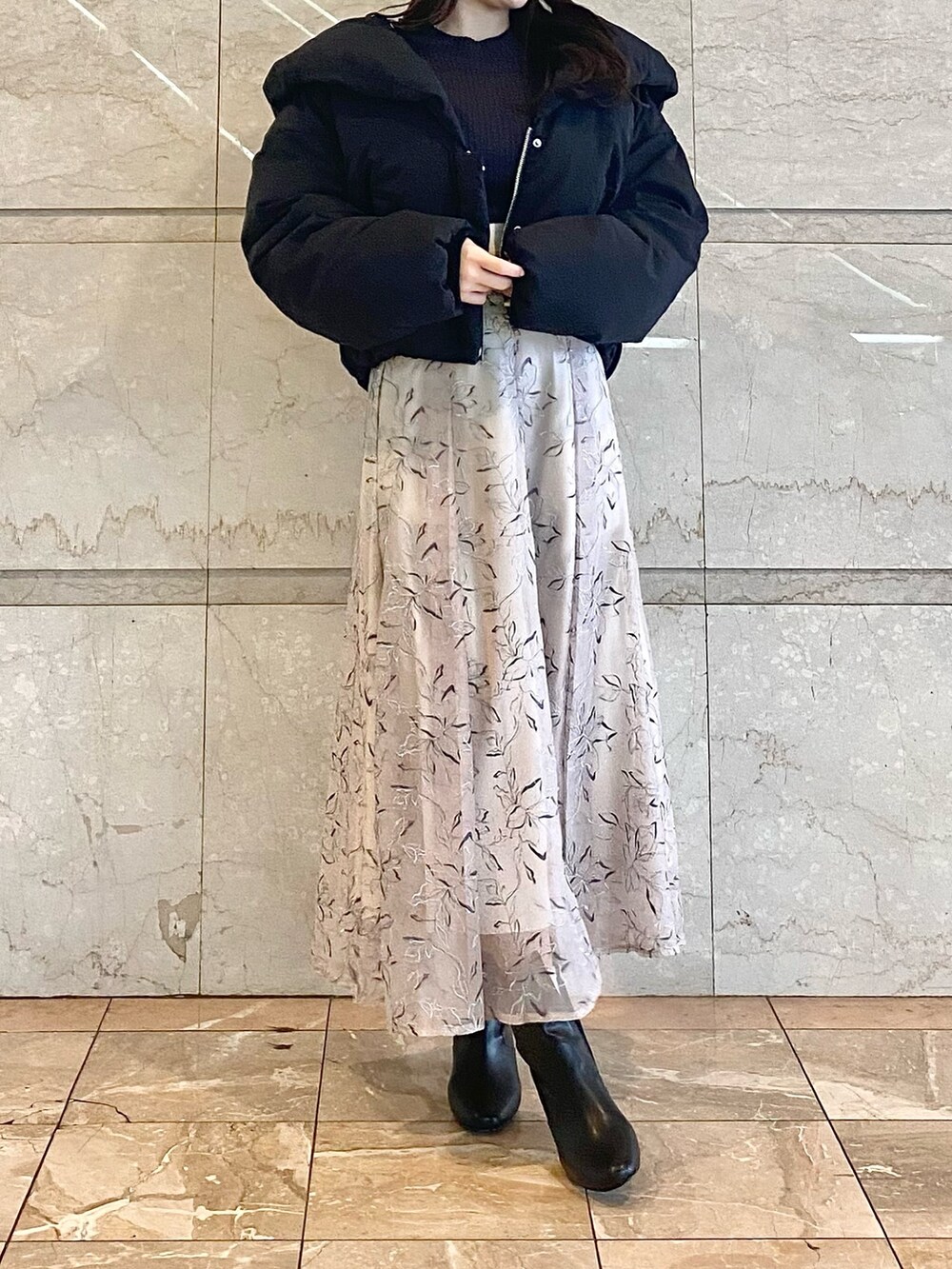 ベージュ系のスカート、グレー系のニット/セーター、ブラック系のダウンジャケット/コートを着用したレディースの冬コーディネートの2枚目の写真