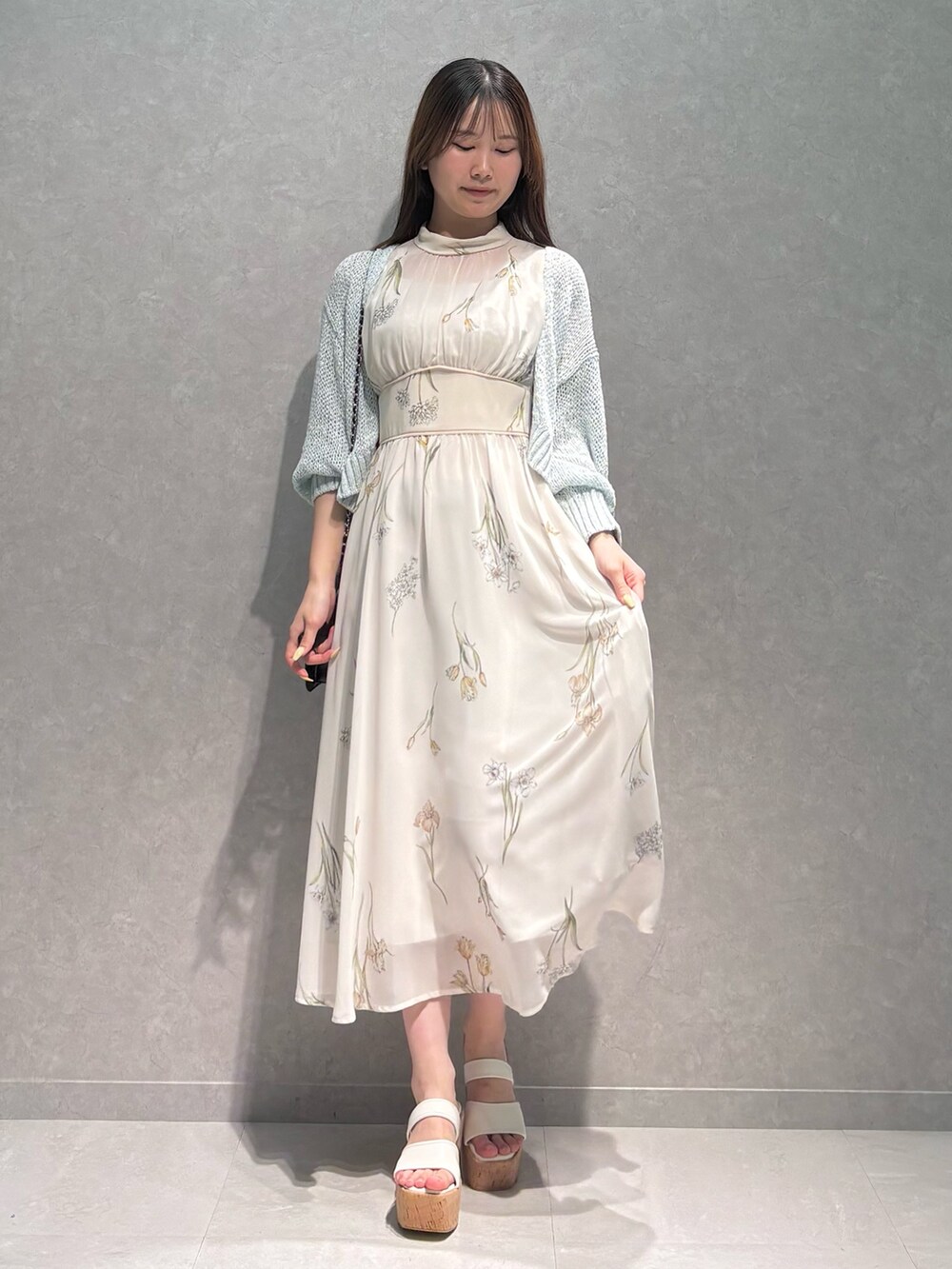ホワイト系のワンピース、ブルー系のカーディガン/ボレロ、ブラック系のハンドバッグを着用したレディースの春コーディネートの2枚目の写真