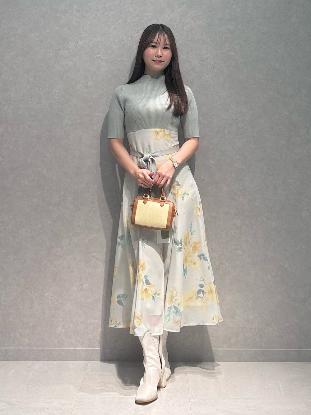 グリーン系のワンピース、ホワイト系のブーツ、ブラウン系のハンドバッグを着用したレディースの春コーディネートの2枚目の写真