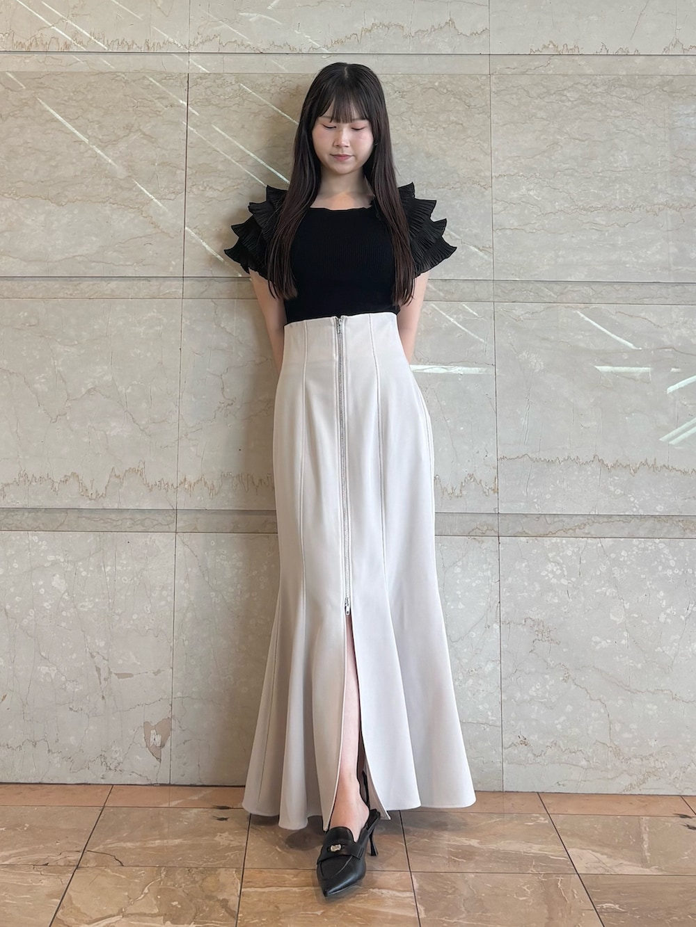 グレー系のスカート、ブラック系のニット/セーター、ブラック系のパンプスを着用したレディースの夏コーディネートの2枚目の写真