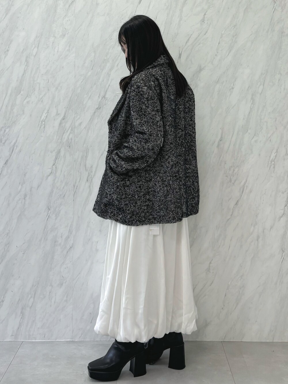 ブラック系のテーラードジャケット、ブラック系のニット/セーター、ホワイト系のスカートを着用したレディースの秋コーディネートの2枚目の写真
