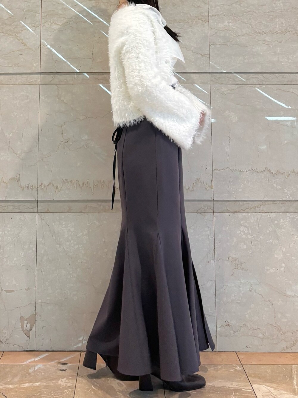 グレー系のスカート、ブラウン系のブーツ、ホワイト系のニット/セーターを着用したレディースの冬コーディネートの3枚目の写真