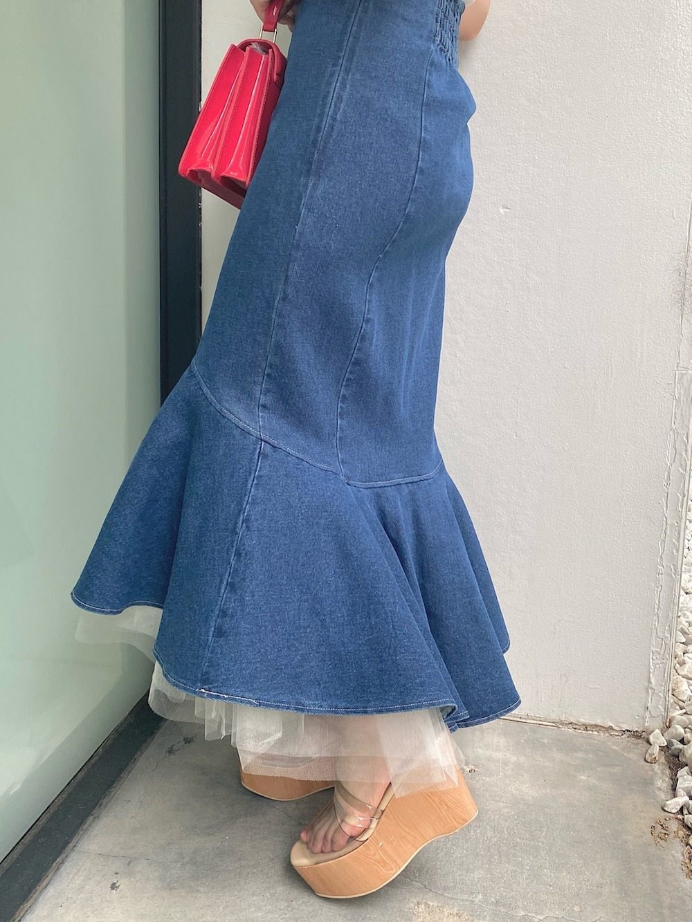 レッド系のハンドバッグ、ブルー系のスカート、ホワイト系のニット/セーターを着用したレディースの夏コーディネートの3枚目の写真