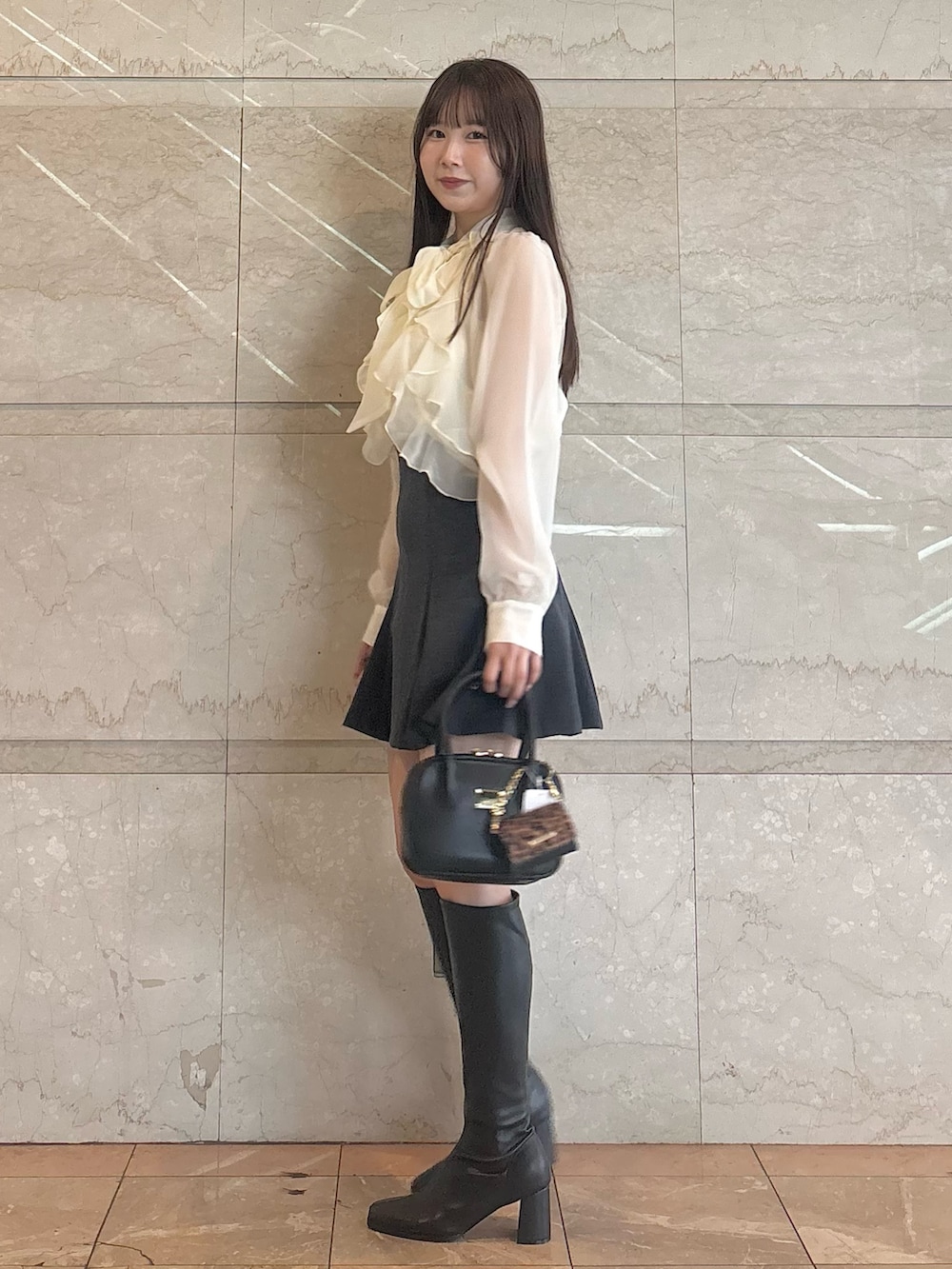 グレー系のスカート、ブラック系のブーツ、ブラック系のハンドバッグを着用したレディースの秋コーディネートの3枚目の写真