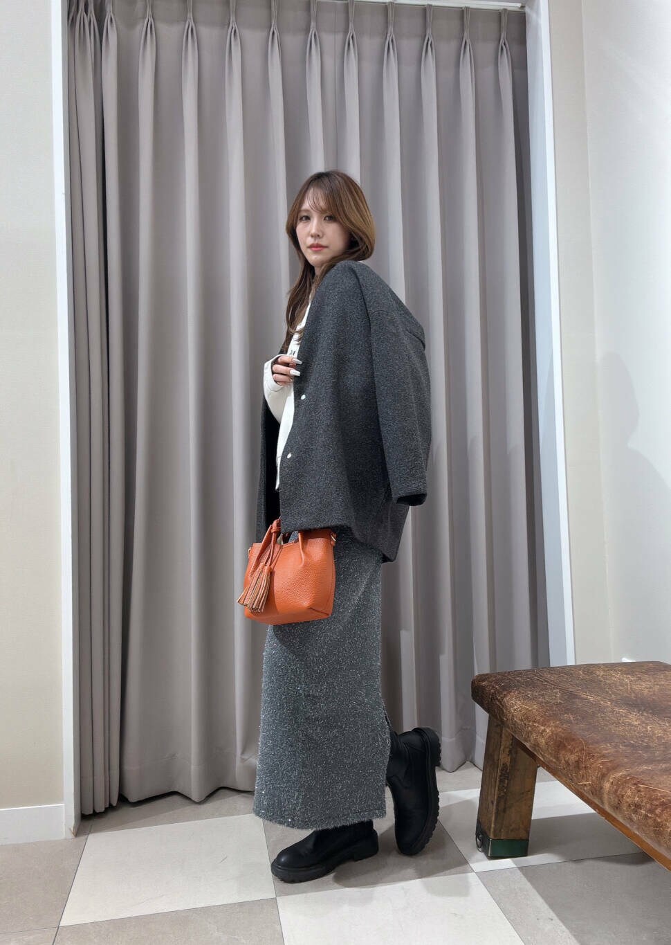 オレンジ系のショルダーバッグ、グレー系のスカート、グレー系のノーカラージャケットを着用したレディースの冬コーディネートの2枚目の写真