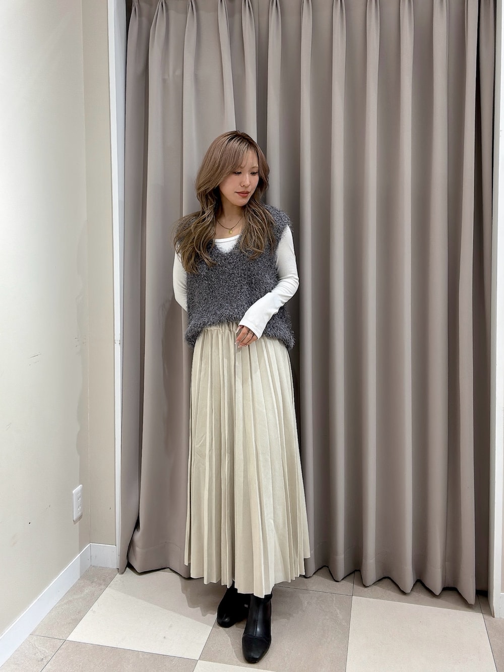 ベージュ系のスカート、グレー系のベストを着用したレディースの冬コーディネートの2枚目の写真