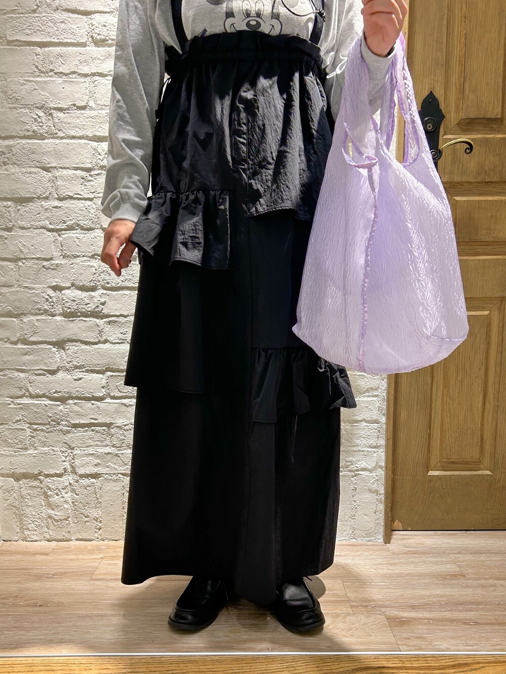 グレー系のTシャツ/カットソー、パープル系のトートバッグ、ブラック系のジャンパースカートを着用したレディースの冬コーディネートの3枚目の写真