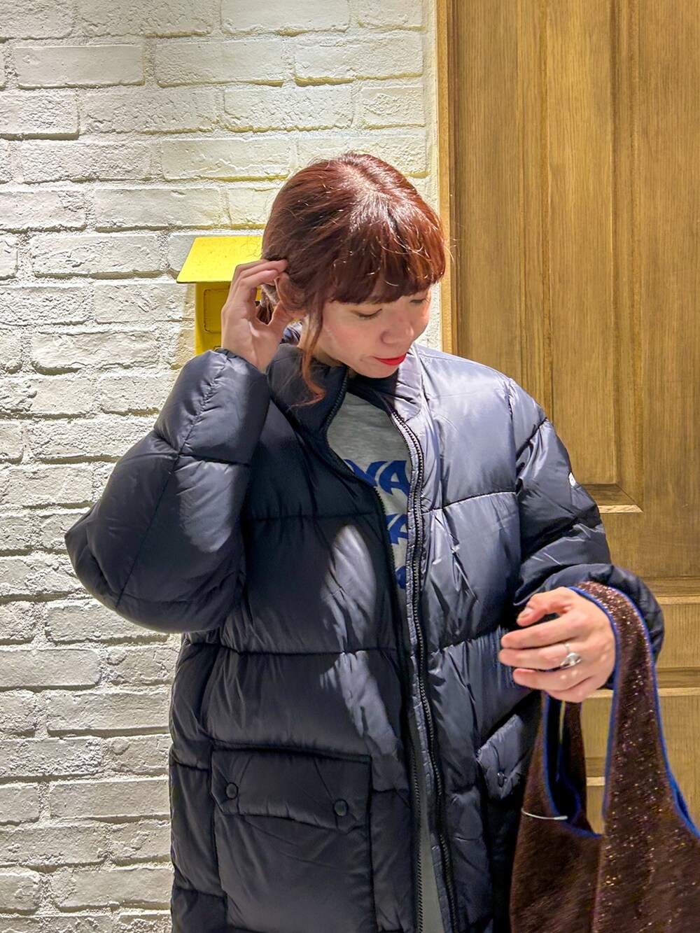 シルバー系のスカート、ブラウン系のショルダーバッグ、ブラック系のダウンジャケット/コートを着用したレディースの秋コーディネートの2枚目の写真