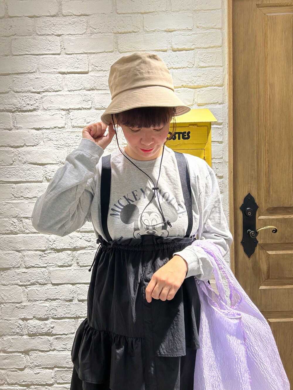 グレー系のTシャツ/カットソー、パープル系のトートバッグ、ブラック系のジャンパースカートを着用したレディースの冬コーディネートの2枚目の写真