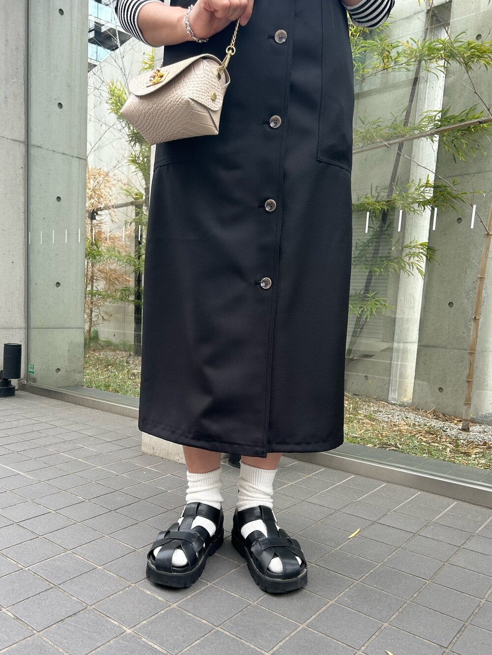 ベージュ系のショルダーバッグ、ブラック系のジャンパースカート、ブラック系のTシャツ/カットソーを着用したレディースの春コーディネートの3枚目の写真