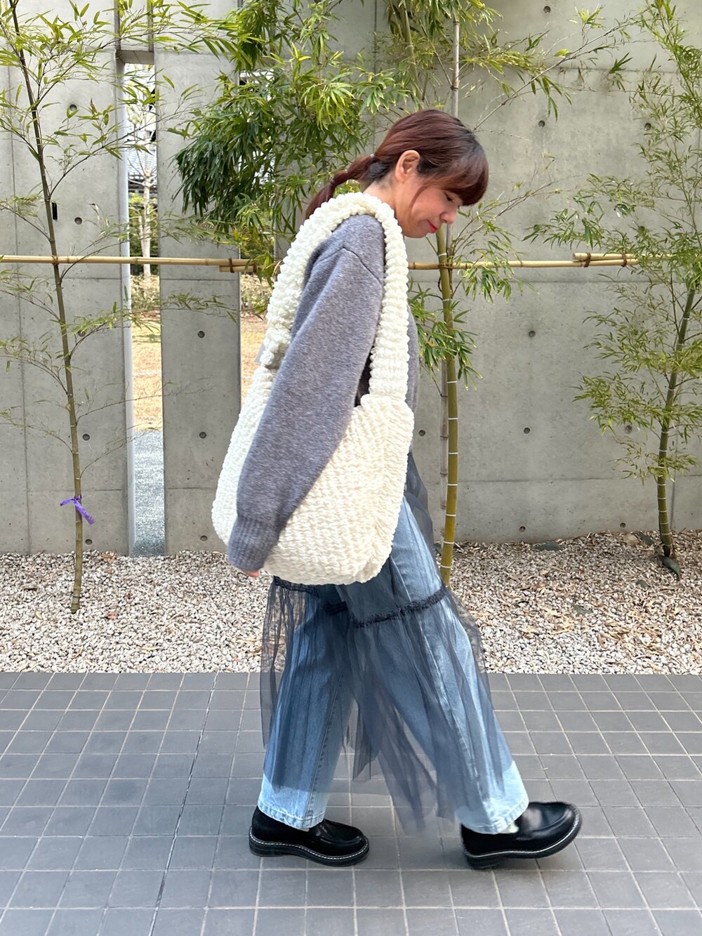 グレー系のニット/セーター、グレー系のスカート、ホワイト系のショルダーバッグを着用したレディースの冬コーディネートの2枚目の写真