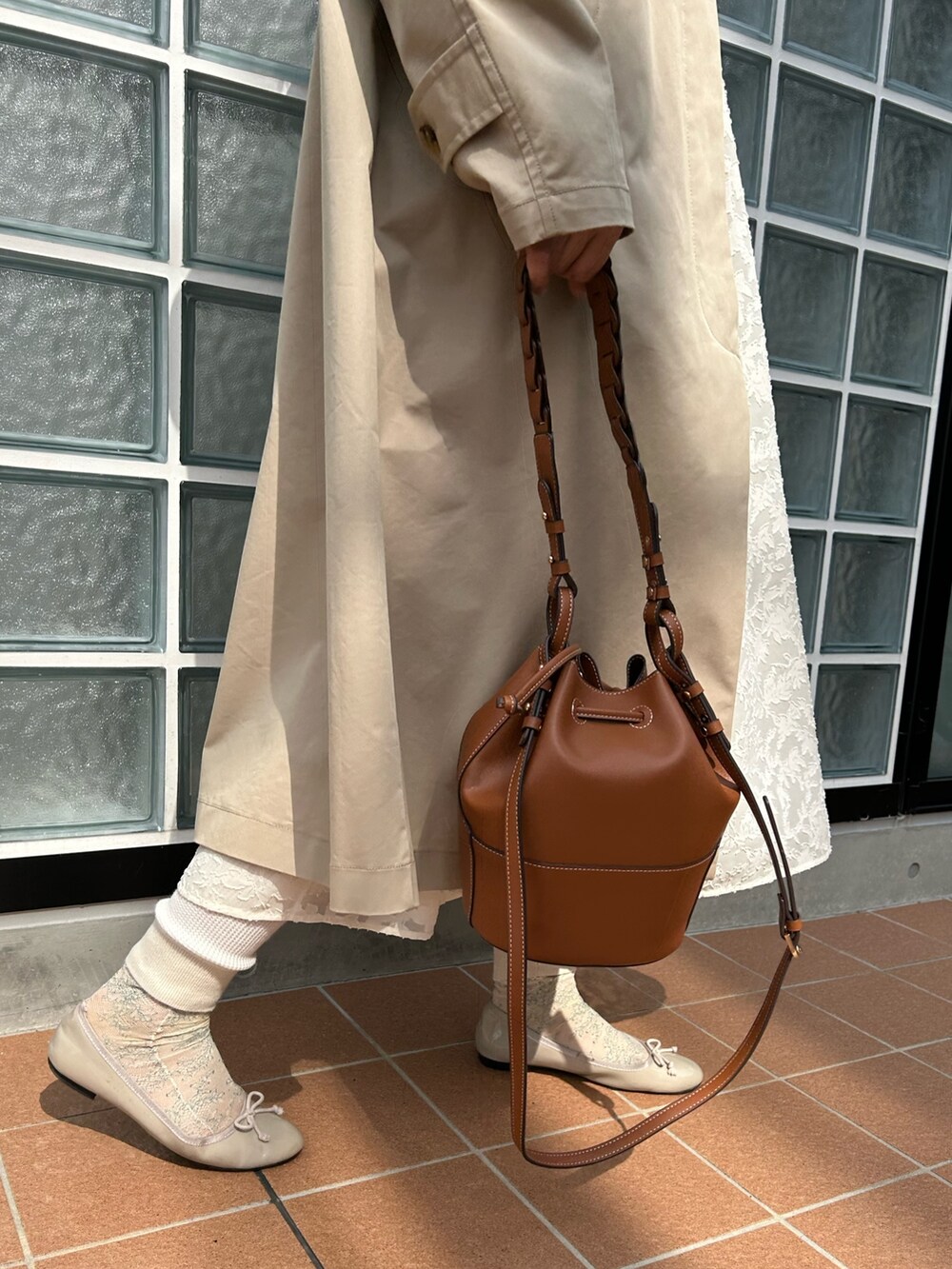 ベージュ系のステンカラーコート、ホワイト系のワンピース、イエロー系のショルダーバッグを着用したレディースの春コーディネートの2枚目の写真