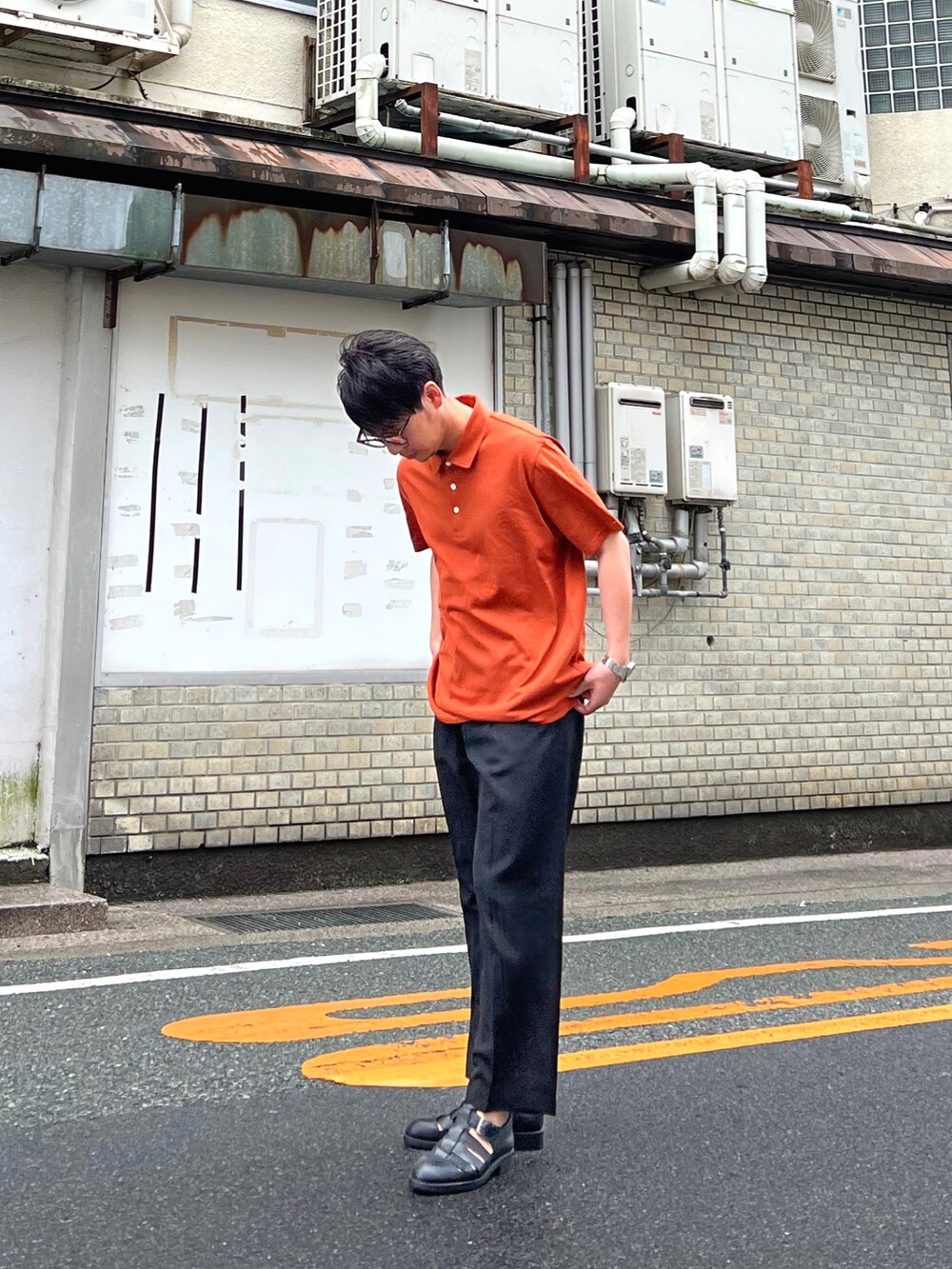 オレンジ系のポロシャツ、ブラック系のパンツ、ブラック系のサンダルを着用したメンズの夏コーディネートの2枚目の写真