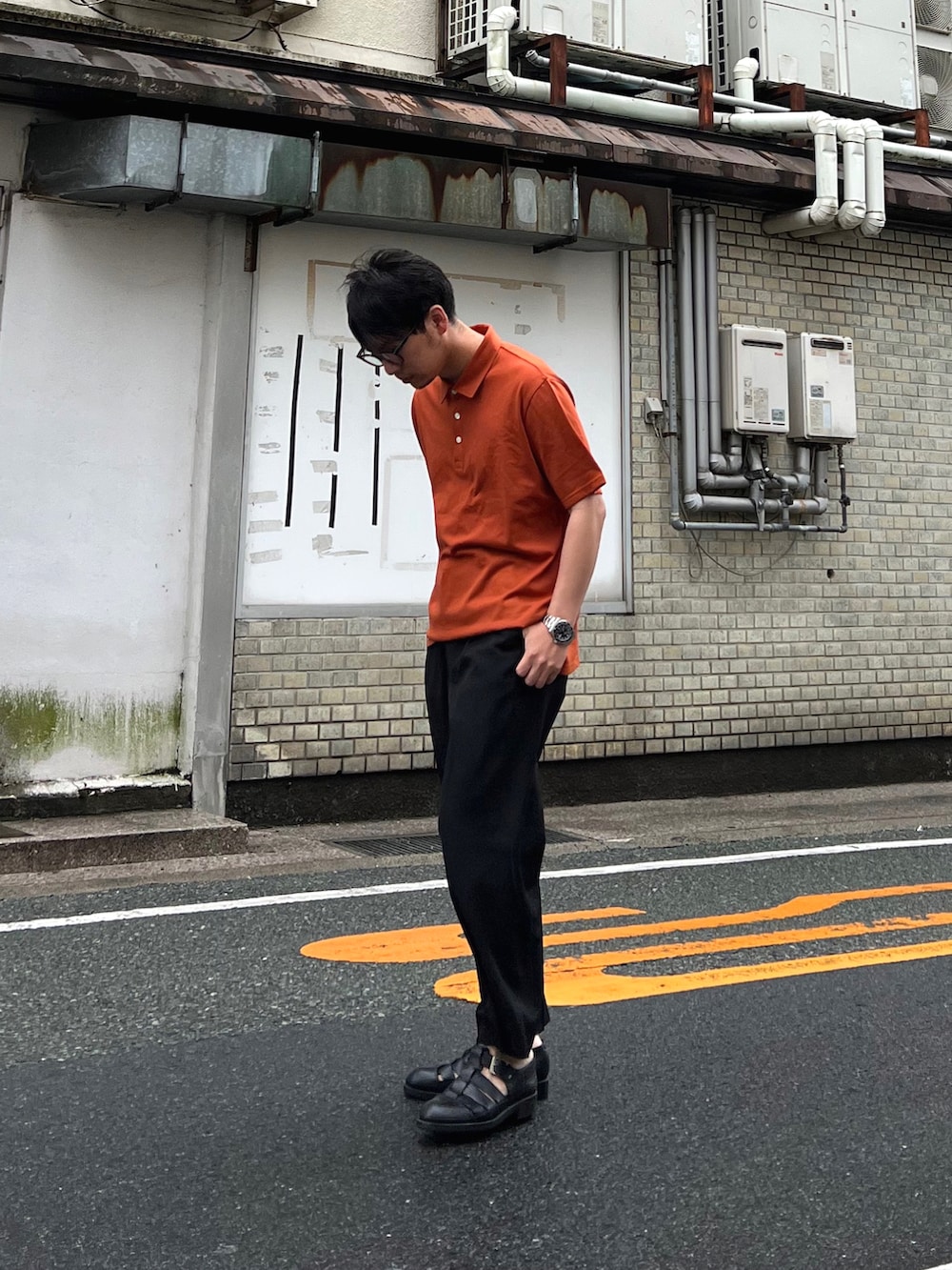 オレンジ系のポロシャツ、ブラック系のパンツ、ブラック系のサンダルを着用したメンズの夏コーディネートの3枚目の写真