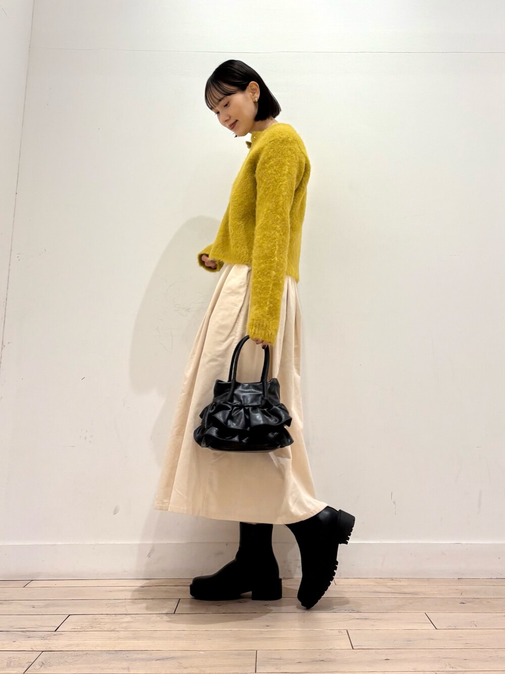 イエロー系のカーディガン/ボレロ、ブラック系のブーツ、ホワイト系のスカートを着用したレディースの秋コーディネートの2枚目の写真