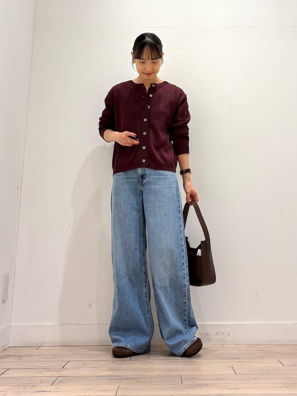 レッド系のカーディガン/ボレロ、ブルー系のデニムパンツ、ブラウン系のハンドバッグを着用したレディースの秋コーディネートの2枚目の写真
