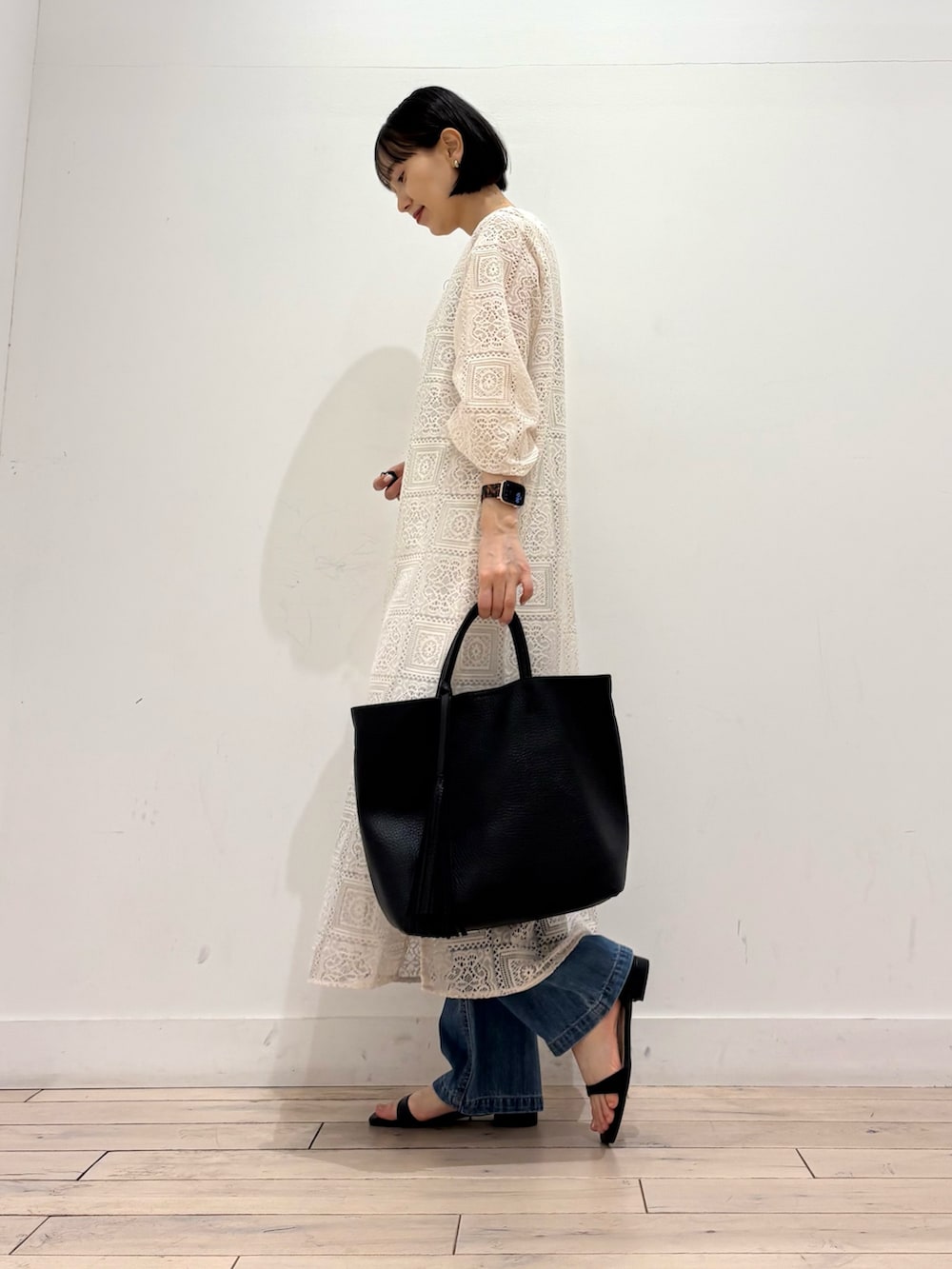 ベージュ系のワンピース、ブルー系のデニムパンツ、ブラック系のトートバッグを着用したレディースの春コーディネートの4枚目の写真
