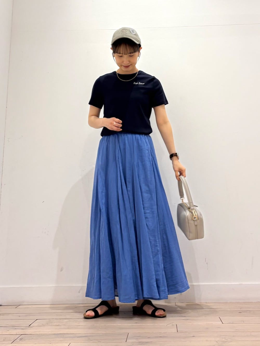 グレー系のショルダーバッグ、ブルー系のスカート、ブラック系のサンダルを着用したレディースの夏コーディネートの2枚目の写真