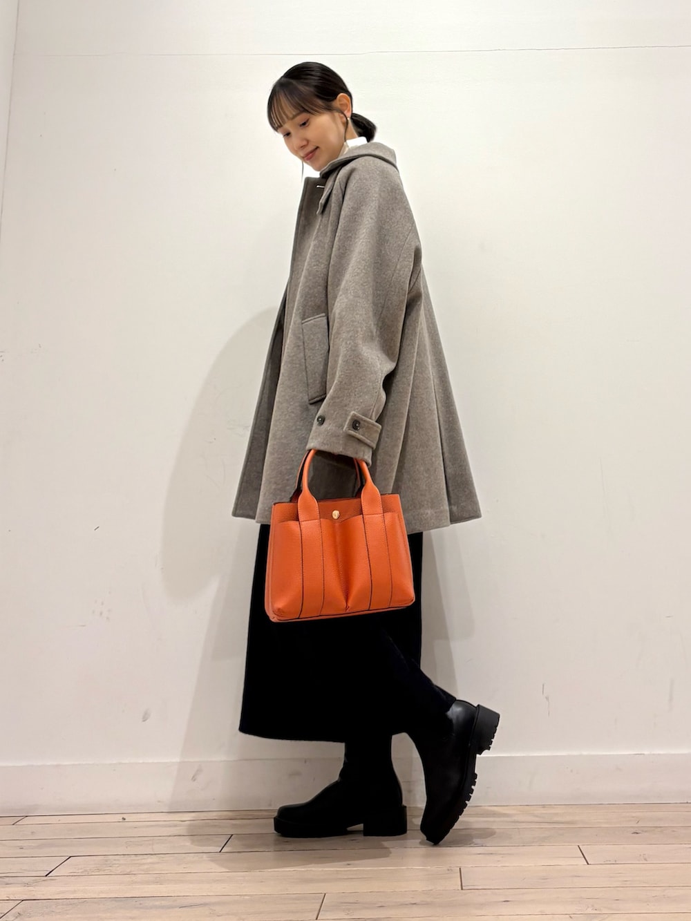 ブラック系のブーツ、オレンジ系のトートバッグ、グレー系のワンピースを着用したレディースの秋コーディネートの2枚目の写真