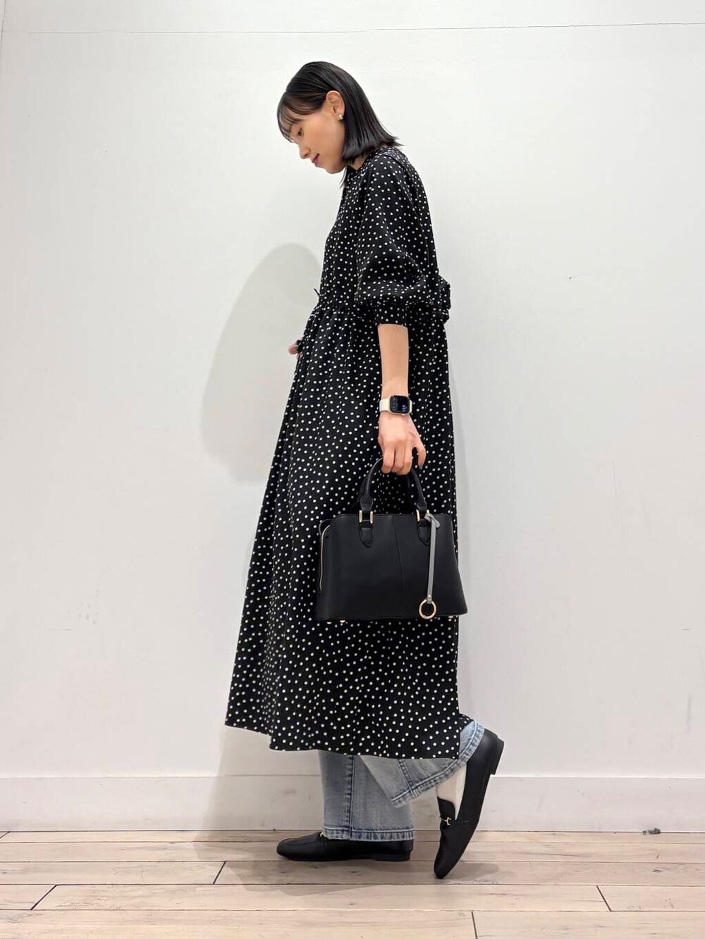 ブラック系のハンドバッグ、ブルー系のデニムパンツ、ブラック系のワンピースを着用したレディースの春コーディネートの2枚目の写真
