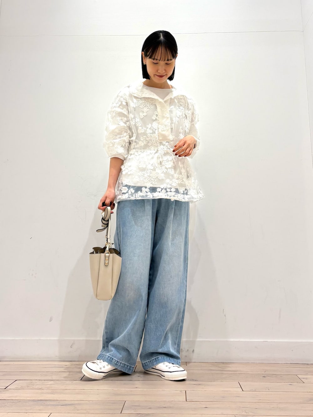 ホワイト系のショルダーバッグ、ホワイト系のスニーカー、ブルー系のデニムパンツを着用したレディースの春コーディネートの2枚目の写真