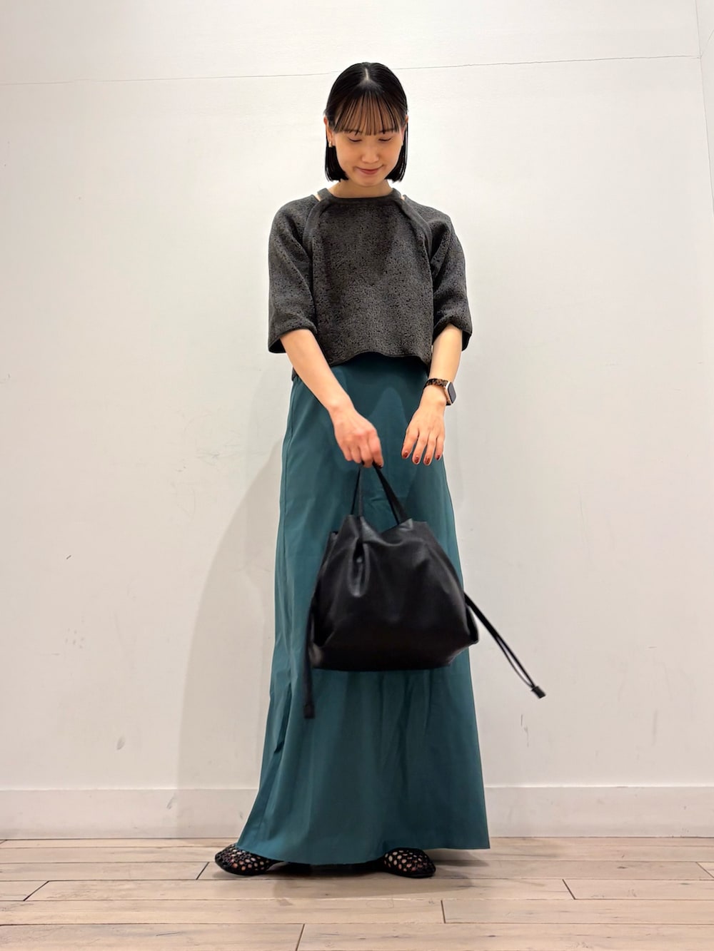 グレー系のニット/セーター、グリーン系のスカート、ブラック系のショルダーバッグを着用したレディースの春コーディネートの2枚目の写真